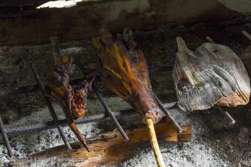 Geräuchertes Fleisch, Unterkiefer und Schädel eines Wildschweines (Sus barbatus), rechts Hüllblätter einer Palme zum anfächern des Feuers.